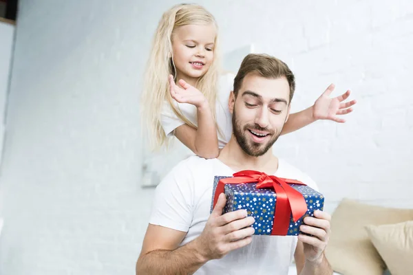 Happy little daughter looking at surprised father holding gift box at home — Stock Photo