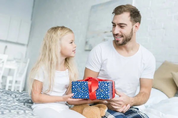Feliz padre e hija sosteniendo caja de regalo y sonriendo entre sí - foto de stock
