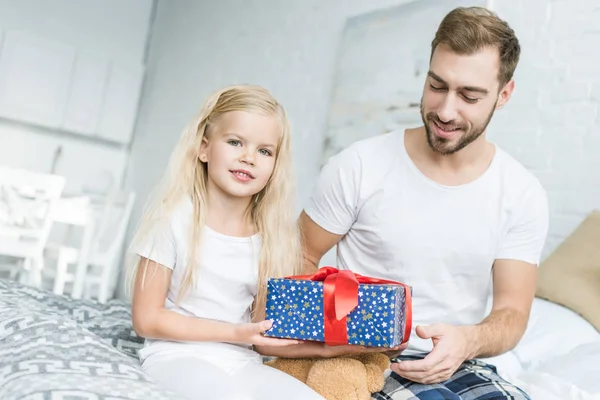 Heureux père regardant mignonne petite fille tenant boîte cadeau à la maison — Photo de stock