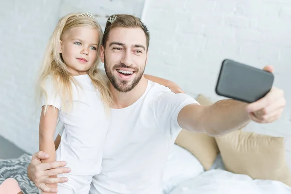 Щасливий батько і мила маленька дочка бере селфі зі смартфоном вдома — стокове фото