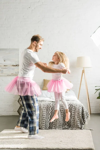Счастливый отец и милая маленькая дочь в розовых юбочках пачки танцуют дома — стоковое фото