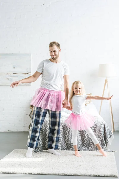 Happy father and adorable little daughter in pink tutu skirts holding hands and dancing together at home — Stock Photo