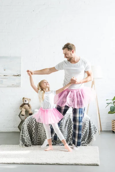 Счастливые отец и дочь в розовых юбочках в пачках, держась за руки и танцуя вместе — стоковое фото