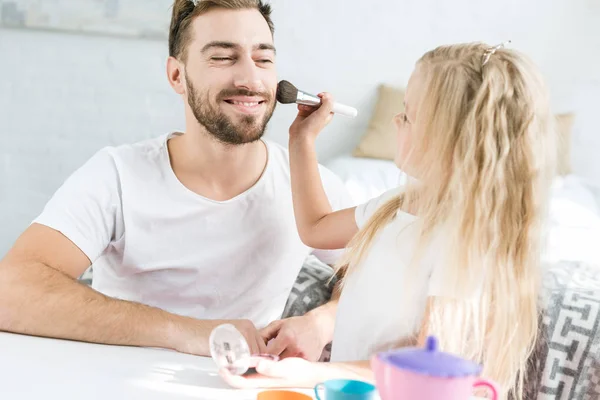 Чарівна маленька дочка застосовує макіяж до щасливого бородатого батька вдома — стокове фото