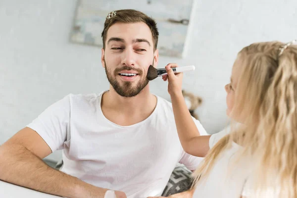 Little daughter applying makeup to smiling bearded father at home — Stock Photo