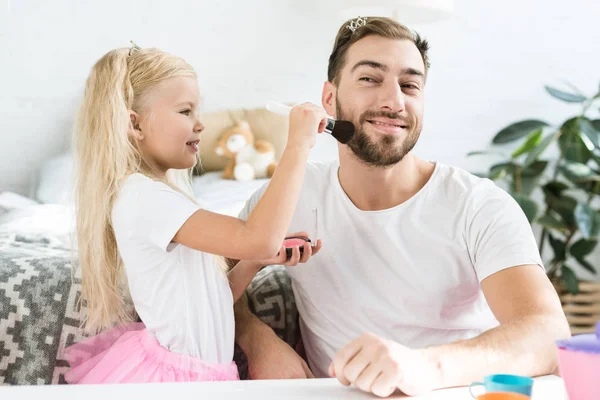 Linda hijita aplicando maquillaje a padre feliz en casa - foto de stock