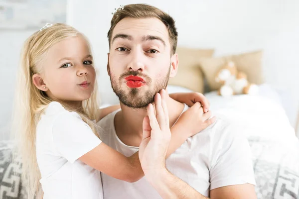 Cute little daughter and bearded father with red lipstick smiling at camera — Stock Photo