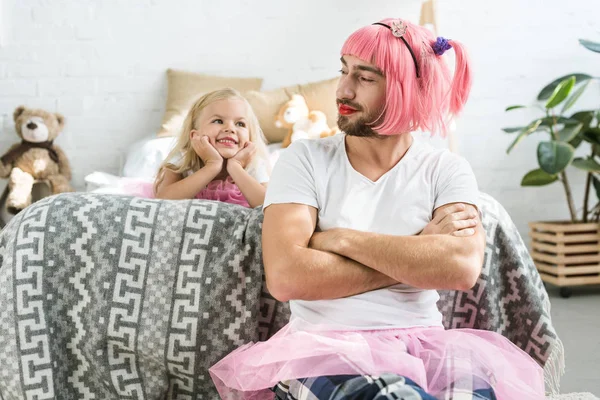 Adorable happy daughter looking at smiling father in pink wig and tutu skirt — Stock Photo
