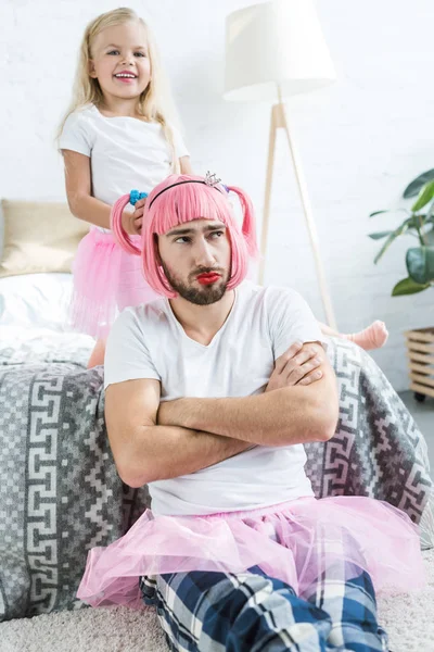 Adorable happy daughter playing with father in pink wig and tutu skirt — Stock Photo