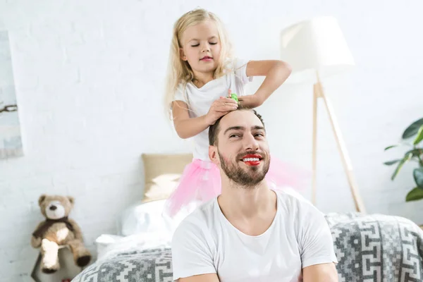 Cute little daughter in pink tutu skirt playing with happy father with red lipstick — Stock Photo
