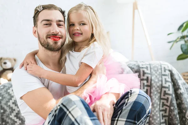 Adorable little daughter in pink tutu skirt hugging happy father with red lipstick — Stock Photo