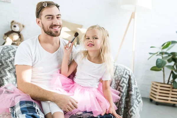 Lindo niño pequeño en rosa tutú falda aplicación de maquillaje a feliz padre - foto de stock