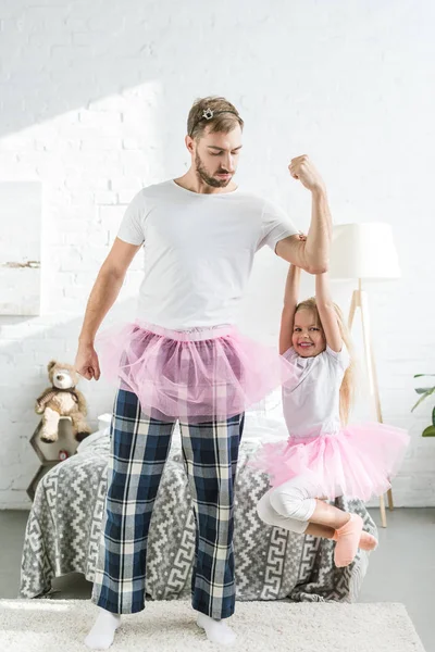 Padre y adorable hijita en faldas tutú rosadas divirtiéndose en casa - foto de stock