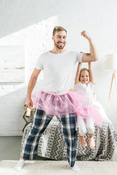 Feliz padre y adorable hijita en rosa tutú faldas bailando y divirtiéndose en casa - foto de stock