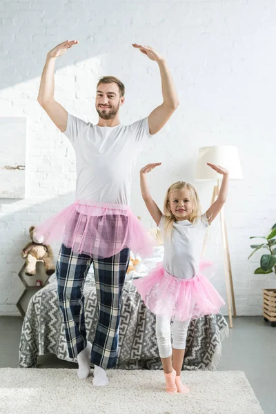 Happy father and adorable little daughter in pink tutu skirts dancing and smiling at camera — Stock Photo