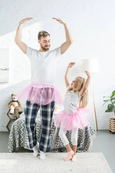 Happy father and adorable little daughter in pink tutu skirts dancing and smiling each other — Stock Photo