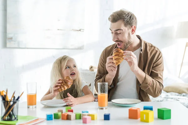 Father and daughter eating croissants and looking at each other — Stock Photo
