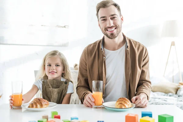 Pai feliz e linda filhinha sorrindo para a câmera enquanto tomando café da manhã juntos — Fotografia de Stock