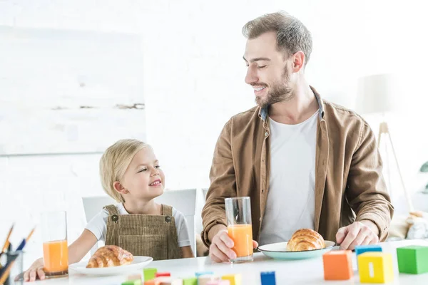 Glücklicher Vater und süße kleine Tochter lächeln sich beim gemeinsamen Frühstück an — Stockfoto