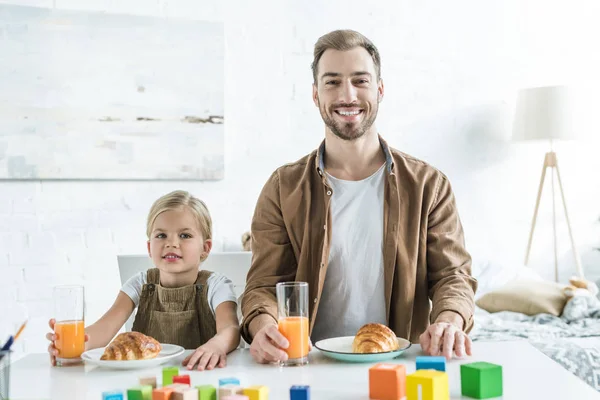Pai feliz e filha sorrindo para a câmera enquanto tomando café da manhã juntos — Fotografia de Stock