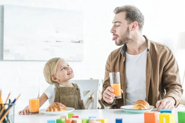 Father showing tongue out to little daughter while having breakfast together — Stock Photo