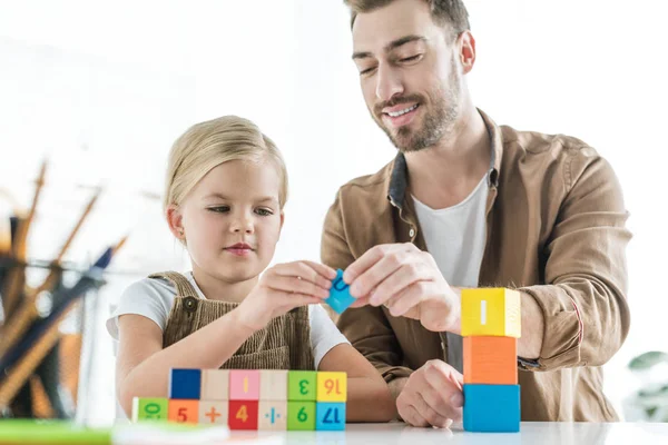 Feliz padre y adorable hijita aprendiendo matemáticas con cubos de colores en casa - foto de stock