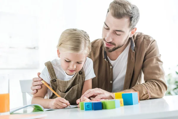 Vater sieht süße kleine Tochter in Arbeitsbuch schreiben und zu Hause lernen — Stockfoto