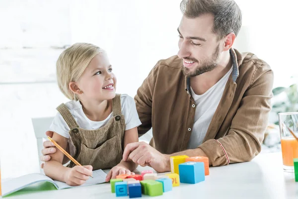 Padre e figlia felici che si sorridono mentre imparano con cubi di legno a casa — Foto stock