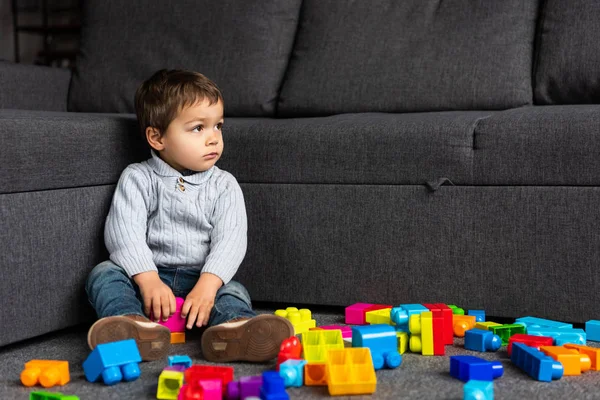 Маленький хлопчик сидить на підлозі з барвистими пластиковими блоками вдома — стокове фото