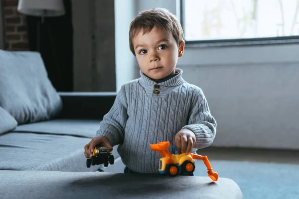 Niño alegre jugando con coches de juguete en la sala de estar en casa - foto de stock