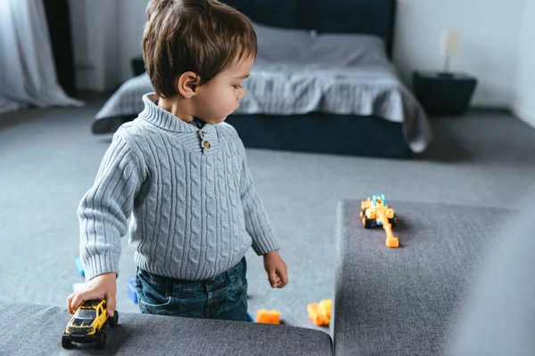 Foco seletivo de menino brincando com carros de brinquedo na sala de estar em casa — Fotografia de Stock