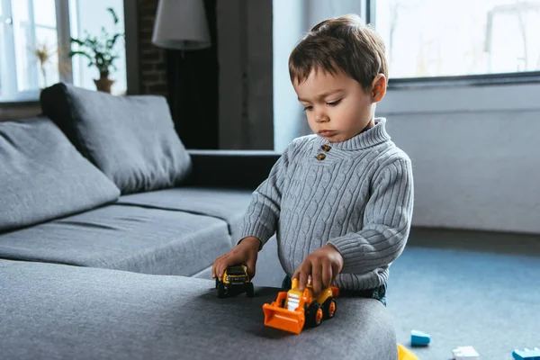 Menino bonito brincando com carros de brinquedo na sala de estar em casa — Fotografia de Stock