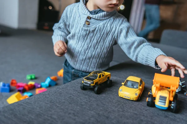 Vue partielle du garçon jouant avec des voitures jouets dans le salon à la maison — Photo de stock