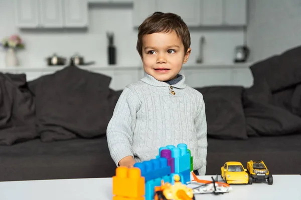 Милий маленький хлопчик грає з іграшковими машинами за столом у вітальні вдома — стокове фото