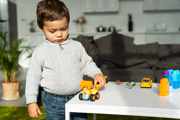 Criança brincando com carros de brinquedo à mesa na sala de estar em casa — Fotografia de Stock