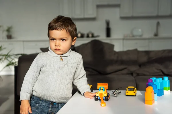 Serious playing with toy cars at table in living room at home — Stock Photo