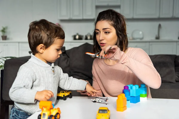 Foco seletivo da mulher brincando com avião de brinquedo perto do filho em casa — Fotografia de Stock