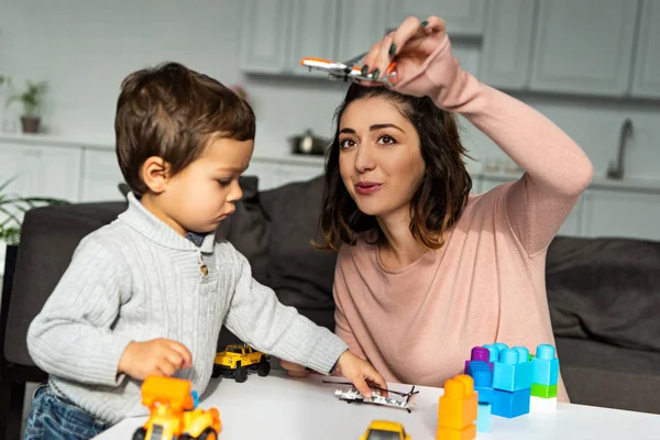 Allegra madre che gioca con l'aeroplano giocattolo vicino al piccolo figlio a casa — Foto stock