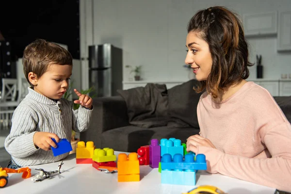 Маленький мальчик и его мать играют с красочными пластиковыми блоками дома — стоковое фото