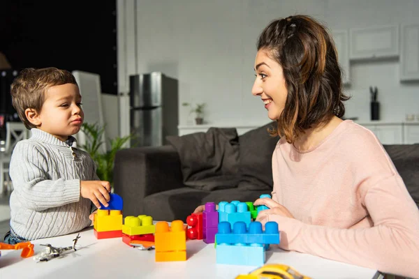 Glückliche Mutter und kleiner Sohn spielen zu Hause mit bunten Plastikklötzen — Stockfoto