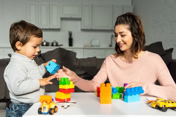 Mãe alegre e pequeno filho brincando com blocos de plástico coloridos em casa — Fotografia de Stock