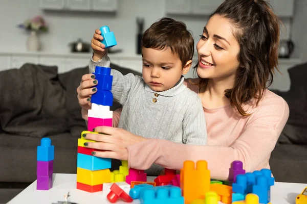 Fröhliche Mutter und kleiner Sohn spielen zu Hause mit bunten Plastikklötzen — Stockfoto