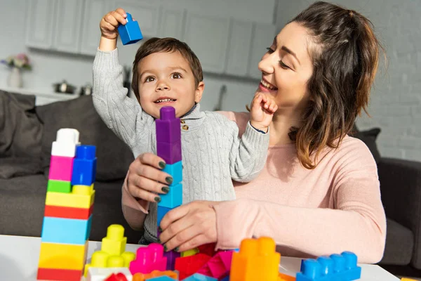 Очаровательный мальчик и его мать играют с красочными пластиковыми блоками дома — стоковое фото