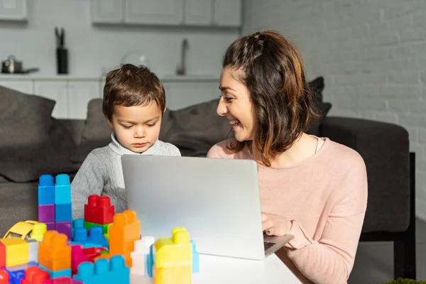 Niño y su madre usando el ordenador portátil en la mesa en la sala de estar en casa - foto de stock