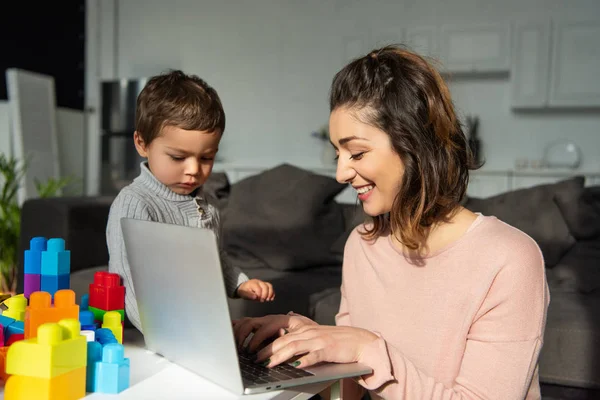 Foyer sélectif du petit garçon et sa mère en utilisant un ordinateur portable à la table dans le salon à la maison — Photo de stock