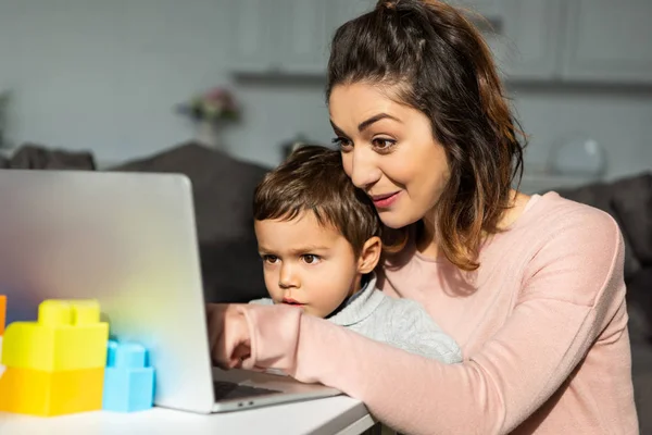 Surpris petit garçon et sa mère en utilisant un ordinateur portable à la table dans le salon à la maison — Photo de stock