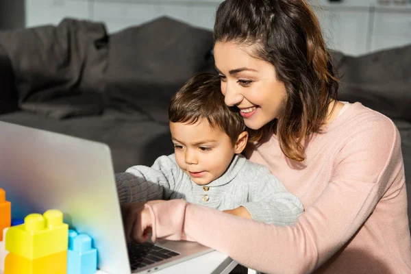 Glücklicher kleiner Junge und seine Mutter mit Laptop am Tisch im heimischen Wohnzimmer — Stockfoto