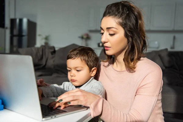 Menino bonito e sua mãe usando laptop na mesa na sala de estar em casa — Fotografia de Stock