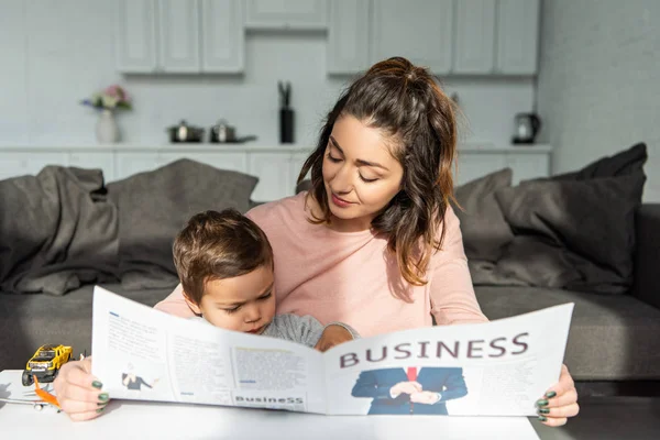 Mère et son petit fils lisant journal d'affaires dans le salon à la maison — Photo de stock