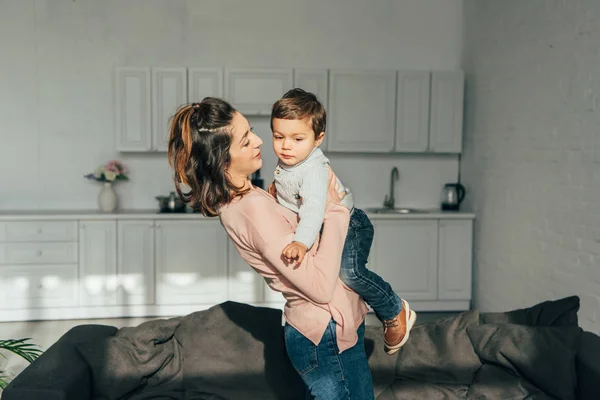 Focalizzazione selettiva di donna allegra che si aggrappa a mani il piccolo figlio a casa — Foto stock